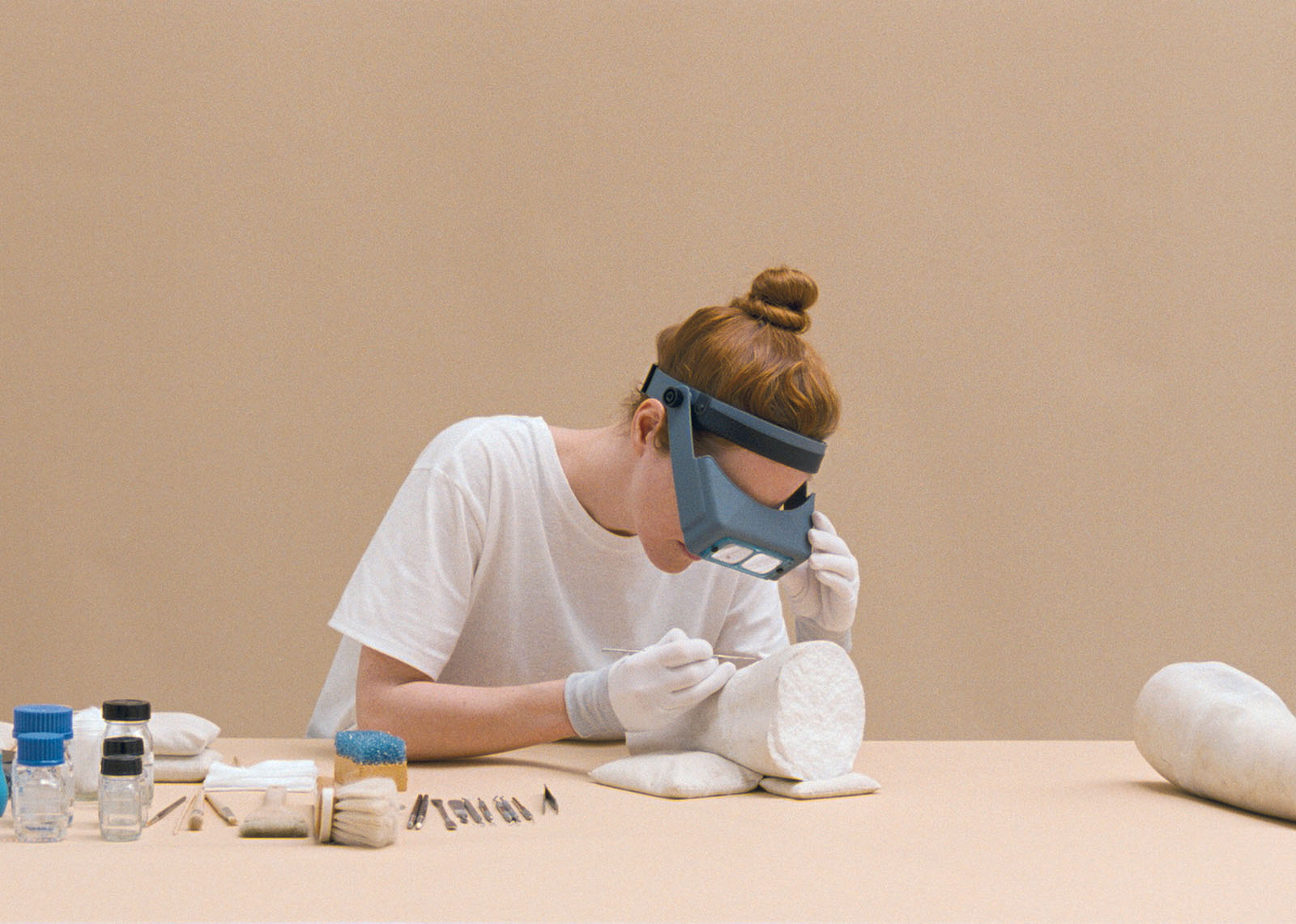 Värivalokuva, jossa valkopaitainen nainen tutkii valkoiset hanskat kädessään valkoista marmoriveistoksen kappaletta.