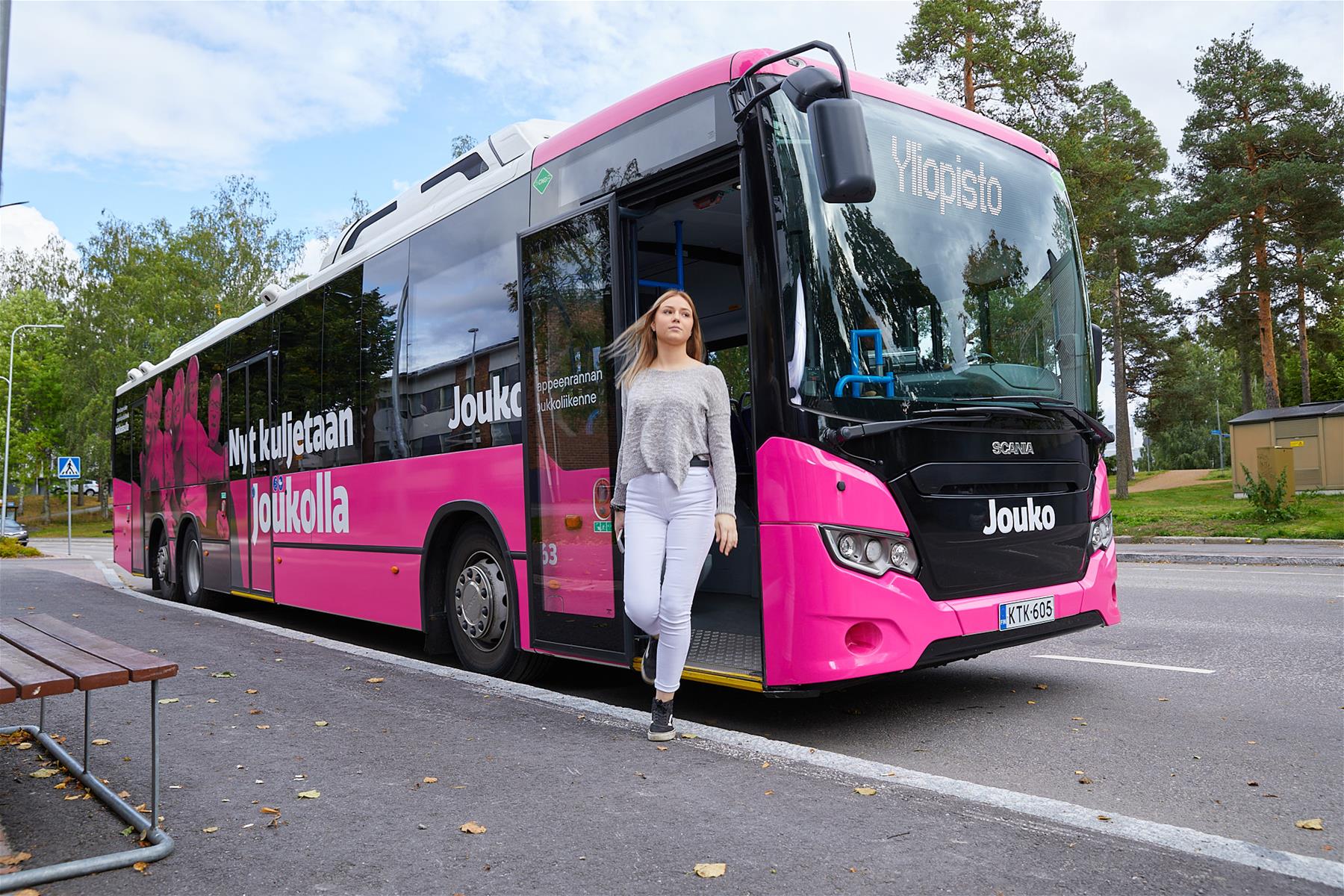 Pinkki Jouko-bussi, bussissa lukee ”Nyt kuljetaan Joukolla, bussin edessä ”Yliopisto”, tyttö astumassa bussista ulos.